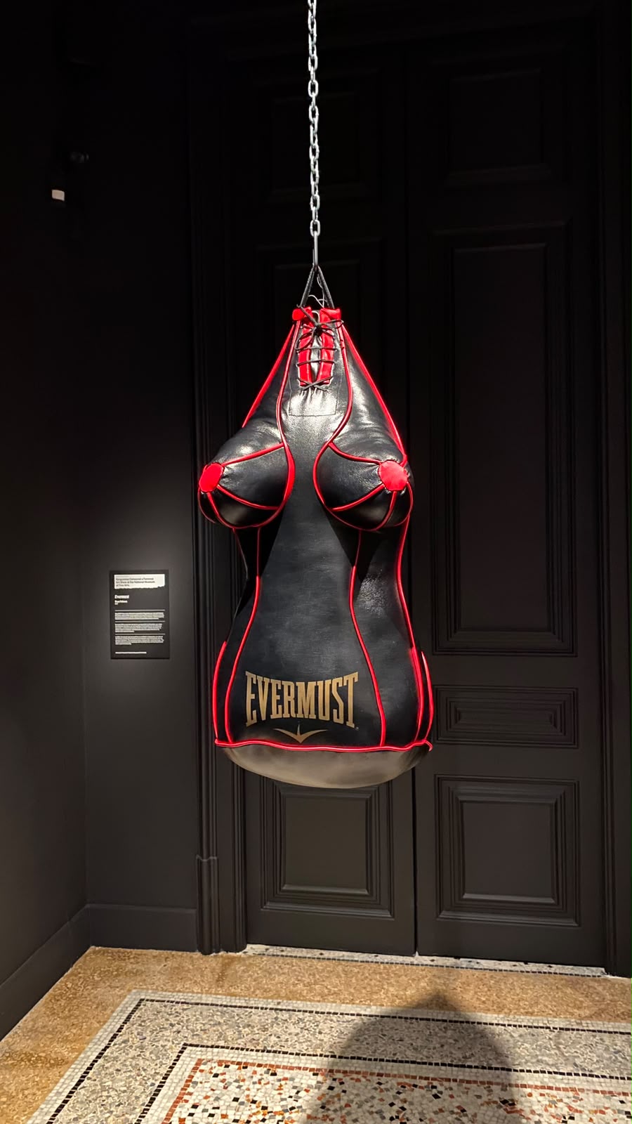 Leather punching bag shaped like a female body hanging in a dark gallery