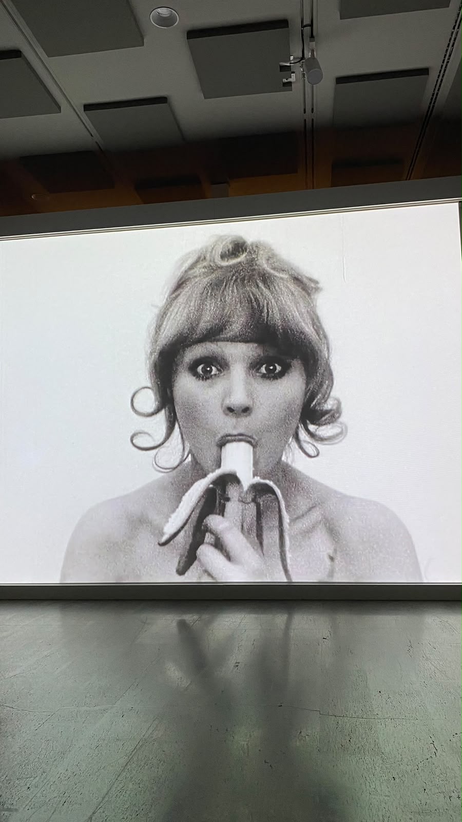 Black-and-white video projection of a woman eating a banana in a gallery
