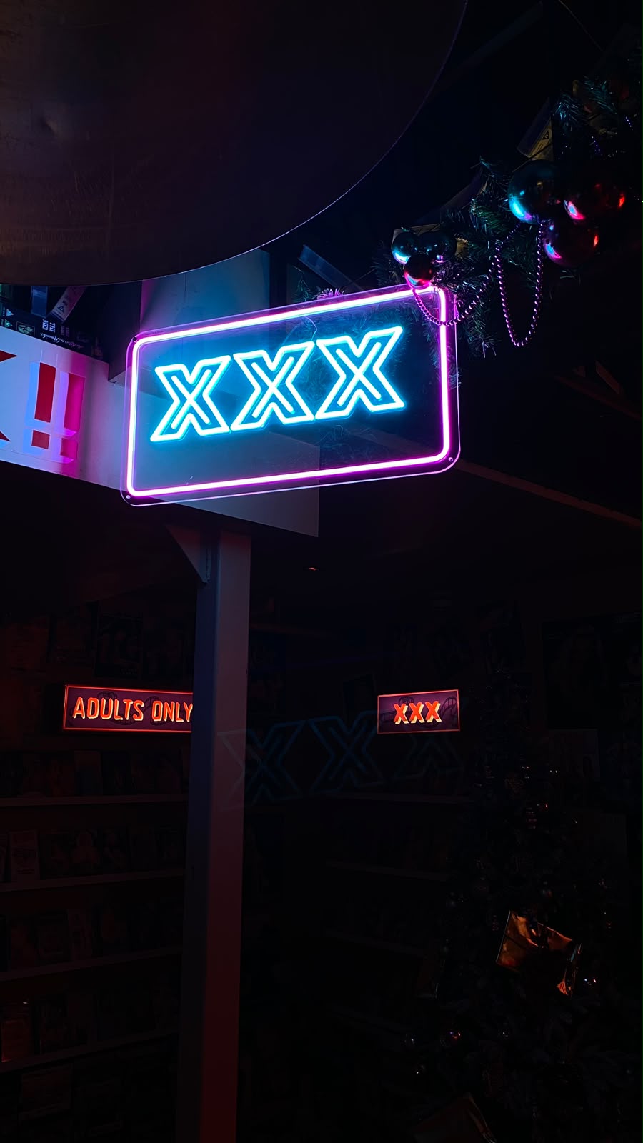 Blue and pink XXX neon sign above shelves of adult films