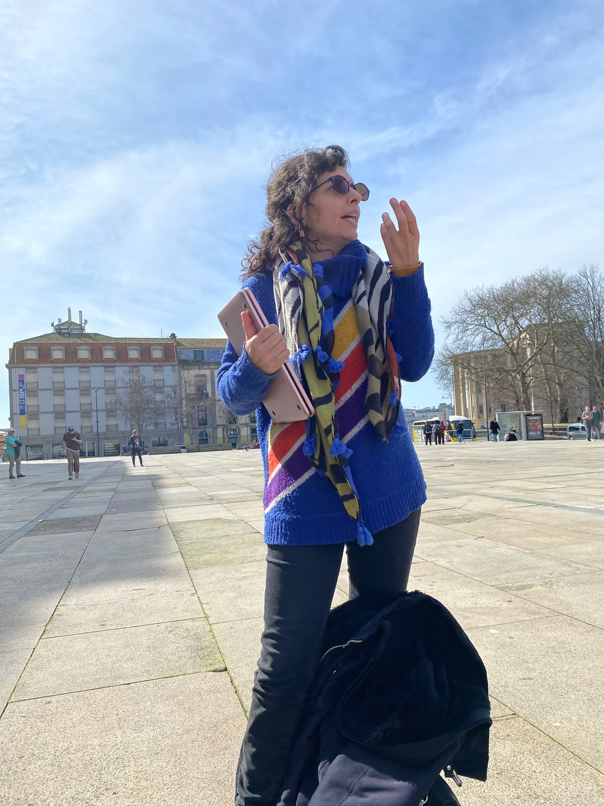 Tour guide in a rainbow-striped jumper speaking in a large square in Porto