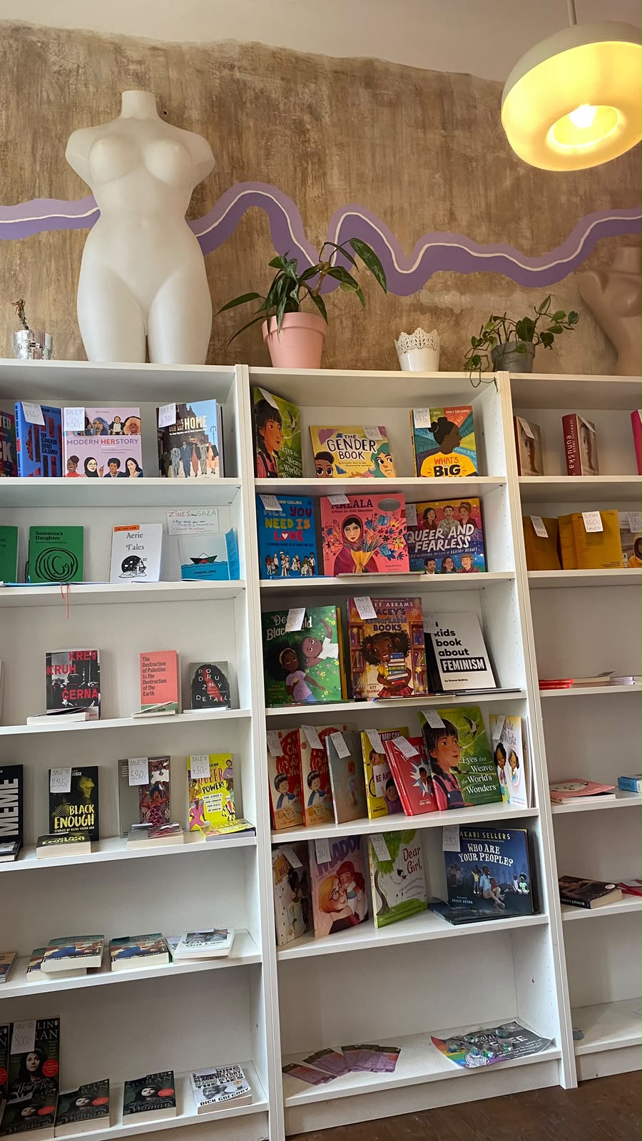 Bookshelves with feminist and queer books under a white sculpture of a female body